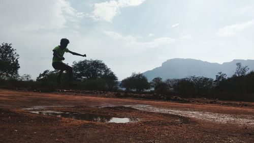 Man walking on dirt road amidst trees against sky