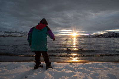 Rear view of man standing on beach during sunset