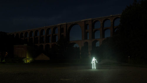 Man against illuminated bridge at night
