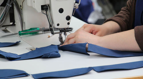 Midsection of tailor using sewing machine while stitching textile