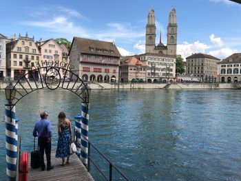 Rear view of people walking on bridge over canal against buildings