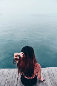 Rear view of woman sitting on pier at sea