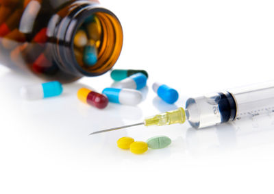 Close-up of syringe with pills and bottle on white background