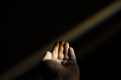 Unrecognizable female hand reaching out to a rainbow in the dark