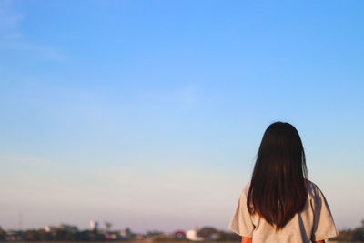 Rear view of young woman sitting against clear sky during sunset