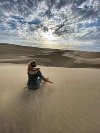 Rear view of woman sitting at desert during sunset