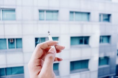 Close-up of hand holding cigarette against building