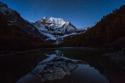Scenic view of lake by snowcapped mountains against sky at night