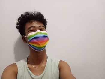 Portrait of boy wearing rainbow masks against white background