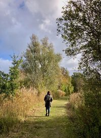 Rear view of woman walking on a grassy footpath between trees and other vegetation