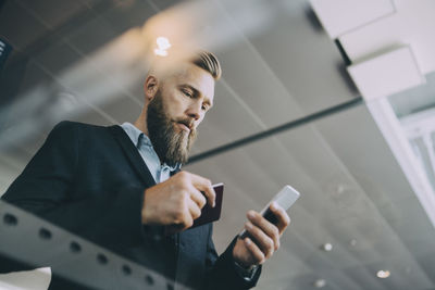 Low angle view of businessman using smart phone while holding passport at airport