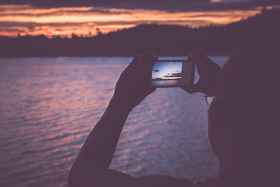 Close-up of man photographing sunset over river in mobile phone