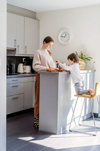 Full length of cute girl with boy preparing food at kitchen