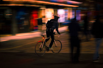 Blurred motion of man riding bicycle on road at night