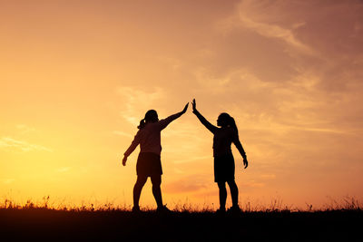 Silhouette friends standing on field against sky during sunset