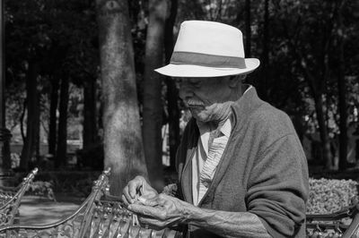 Senior man wearing hat while sitting on bench at park