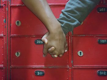 Close up of couple hand holding together in front of red mailboxes