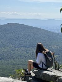 Rear view of woman sitting on mountain against sky