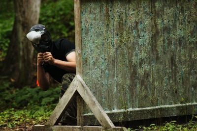 Man wearing mask while kneeling by wood in forest