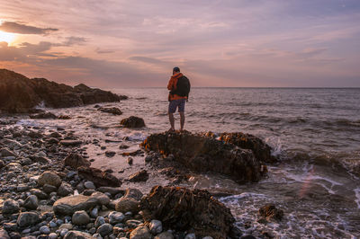 Rear view of man relaxing on rock formation at beach