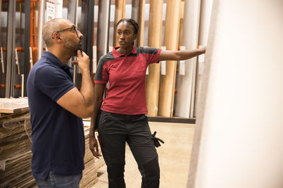 Female sales staff talking to male customer with hand on chin while selecting laminated boards at hardware store