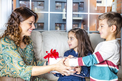 Children giving gift to mother on sofa in living room at home
