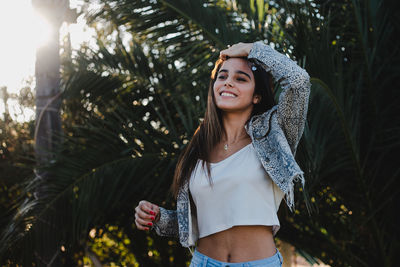 Smiling young woman looking away while standing against trees