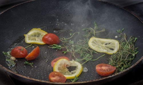 Close-up of herb and lemon slice with cherry tomatoes on cooking pan