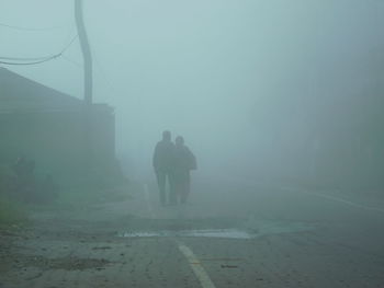 Rear view of people walking on road during foggy weather