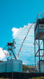 Low angle view of crane by building against blue sky