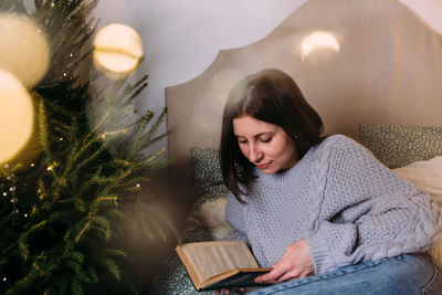 Attractive woman reads a book on the bed in a cozy christmas atmosphere