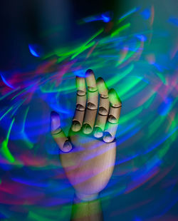 Close-up of human hand against illuminated colored background