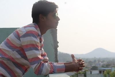 Side view of young man leaning on retaining wall at building terrace