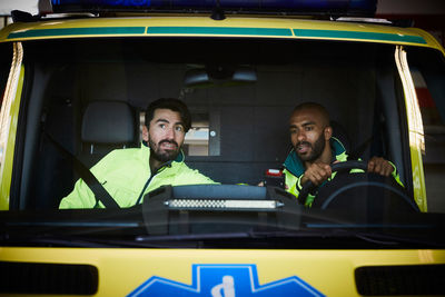 Mid adult male paramedics sitting in ambulance at parking lot