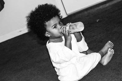 Tilt shot of baby boy drinking from milk bottle while sitting on carpet at home