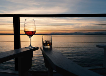 Wine and whiskey on deck chairs at sunset over the sea, landscape.