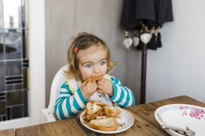 Cute girl eating food on table at home