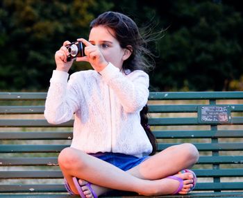 Young woman photographing while sitting on bench