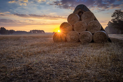 Hay bales on field against sky during sunset