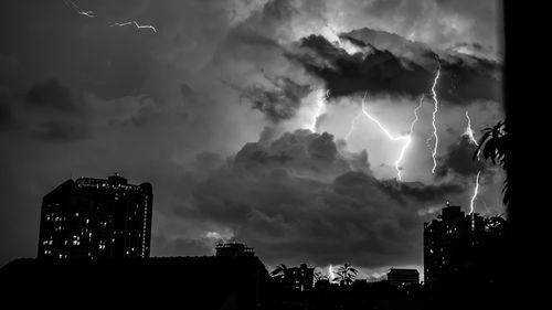 Low angle view of illuminated cityscape against dramatic sky