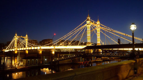 Illuminated bridge over river against sky in city at night