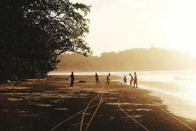 Silhouette people playing soccer on beach against sky during sunset