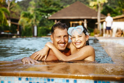 Portrait of smiling daughter and father in swimming pool at tourist resort