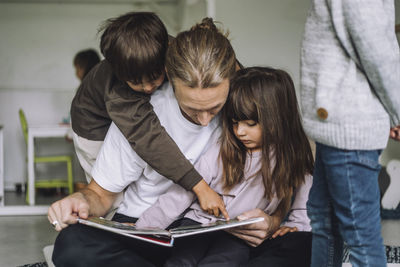 Boy pointing at picture book while male teacher telling story to him at kindergarten