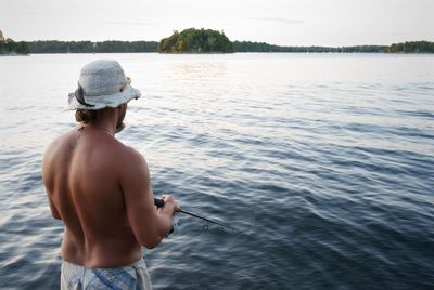 Rear view of shirtless man fishing in lake