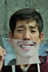 Close-up portrait of boy frowning while holding smiling mask