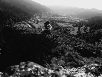 Woman sitting on rocky mountains against sky