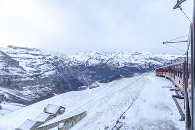 Train by snowcapped mountains against cloudy sky