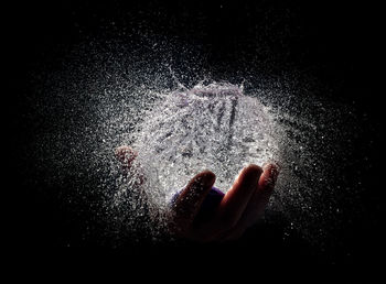 Close-up of hand splashing water against black background