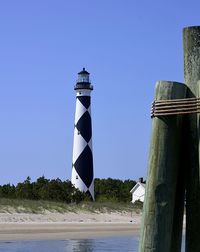 Lighthouse by sea against clear blue sky